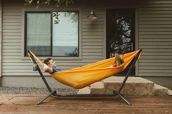 Person relaxing in a yellow hammock in the swiftlet hammock stand on a stand outside a house.