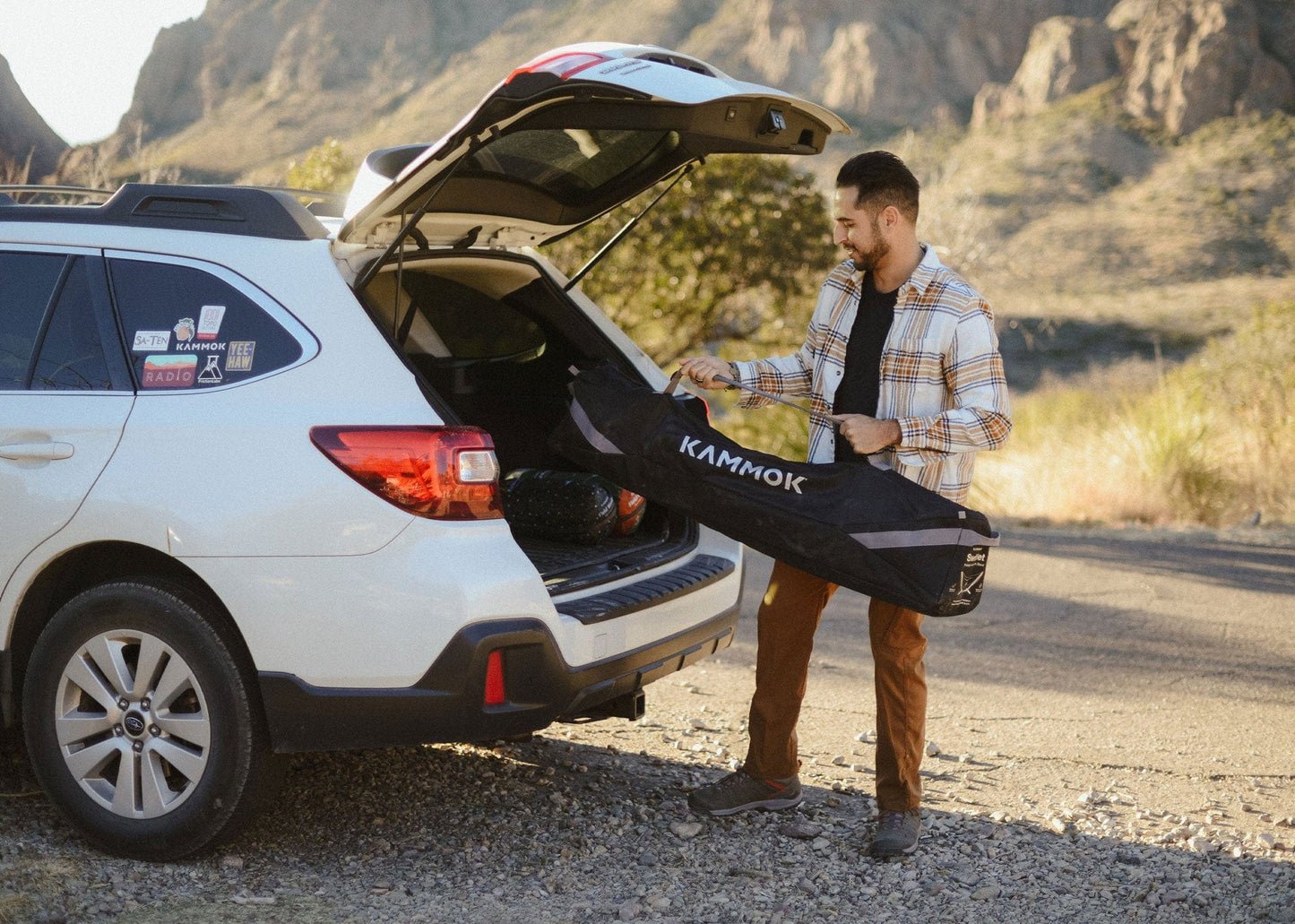 Man loading a Kammok hammock swiftlet stand into the trunk of a car in a desert setting