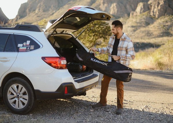 Man loading a Kammok hammock swiftlet stand into the trunk of a car in a desert setting